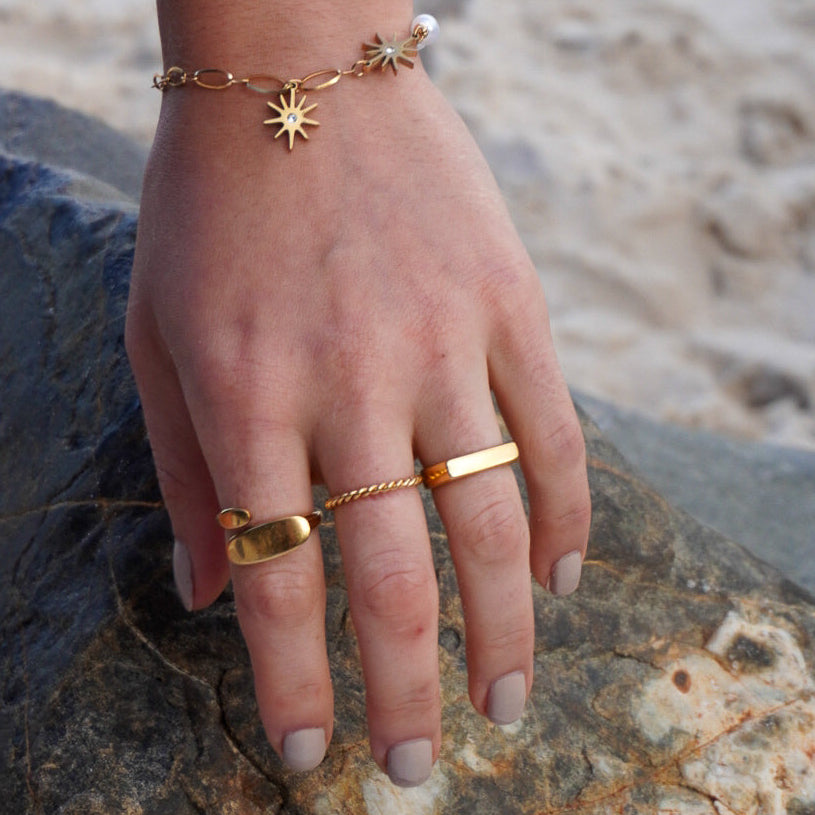 Hand wearing gold rings and bracelets on a rocky surface with a blurred natural background