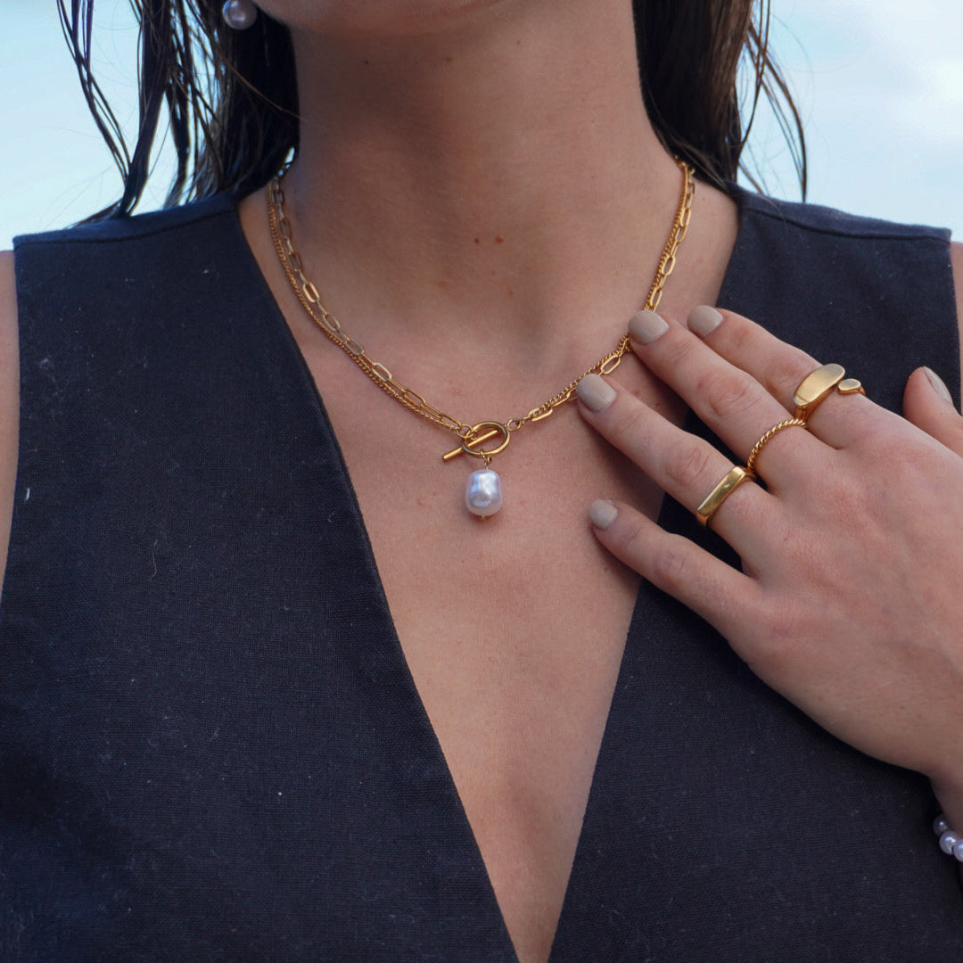 Woman wearing gold necklaces, rings, and a bracelet with a blurred beach background