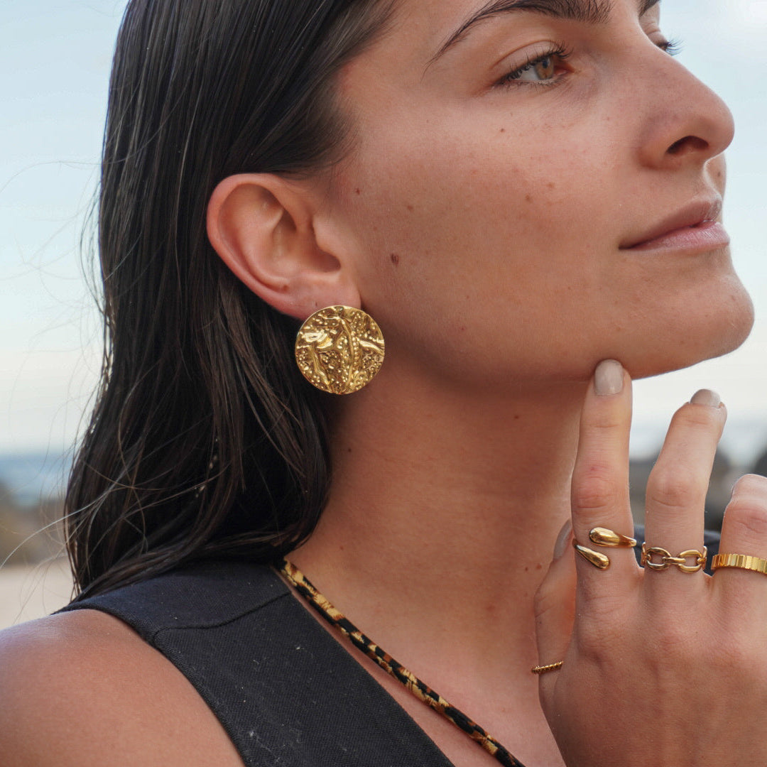 Woman wearing gold earrings and rings outdoors with a blurred natural background