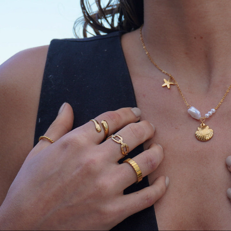 Woman wearing gold jewelry including a necklace, rings, and earrings with a blurred background.