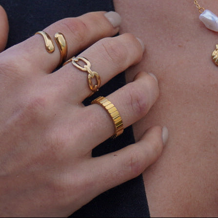 Woman wearing gold jewelry including a necklace, rings, and earrings with a blurred background.