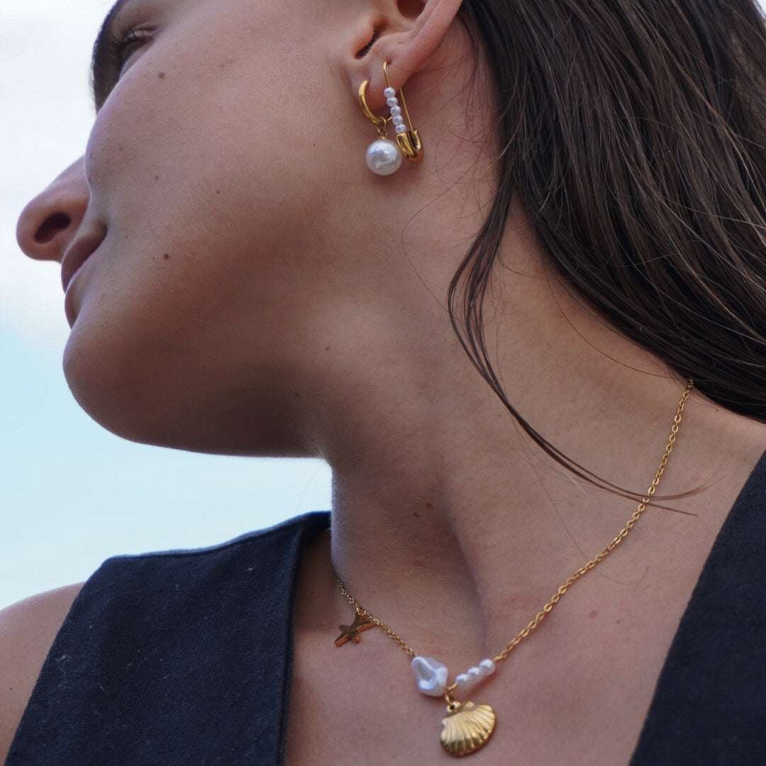 Close-up of a person wearing gold earrings and a necklace with a blue sky background