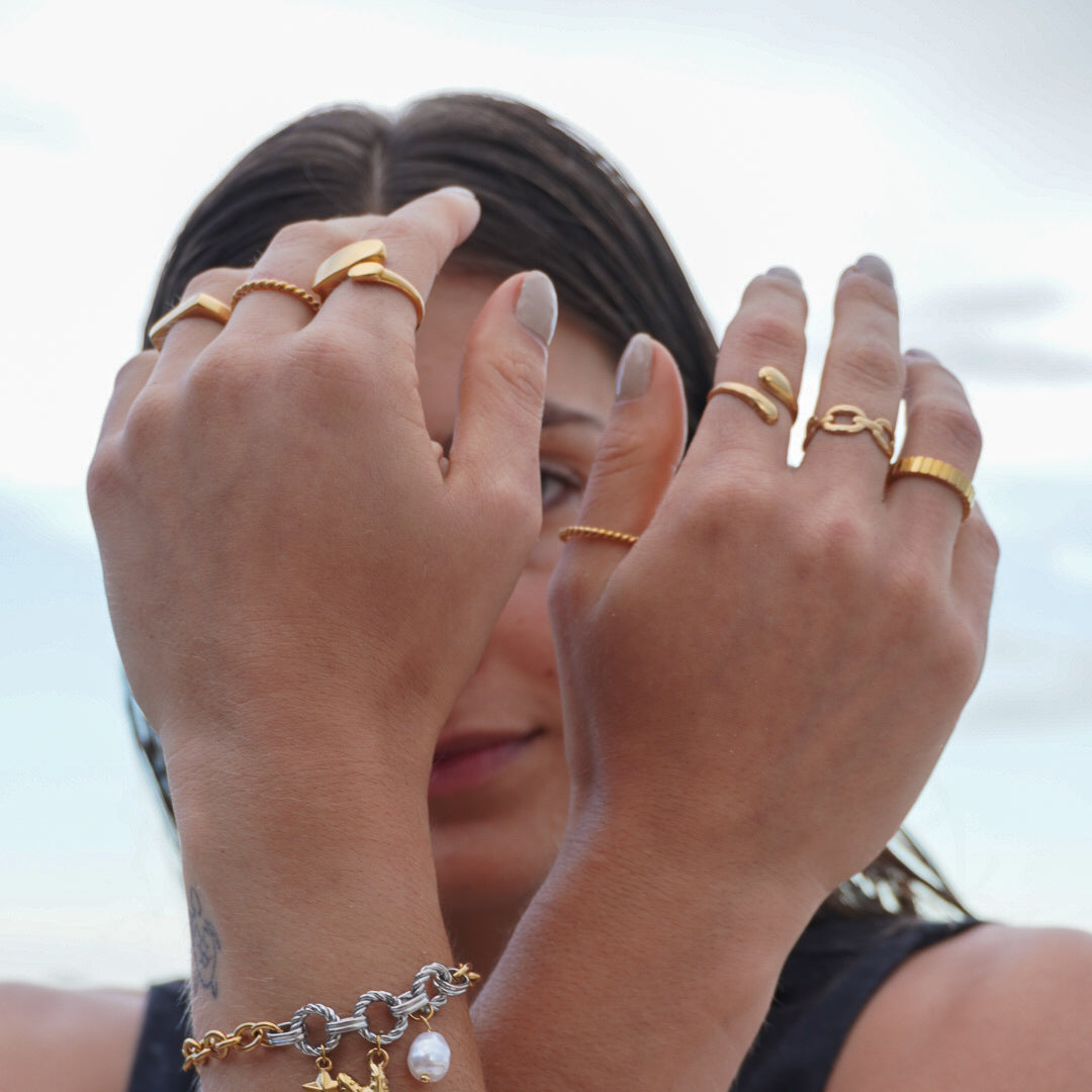Person wearing multiple gold rings and a bracelet with a blurred background