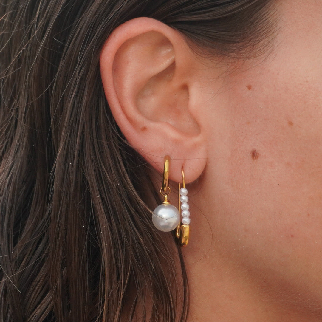 Close-up of an ear wearing gold hoop earrings with pearls.