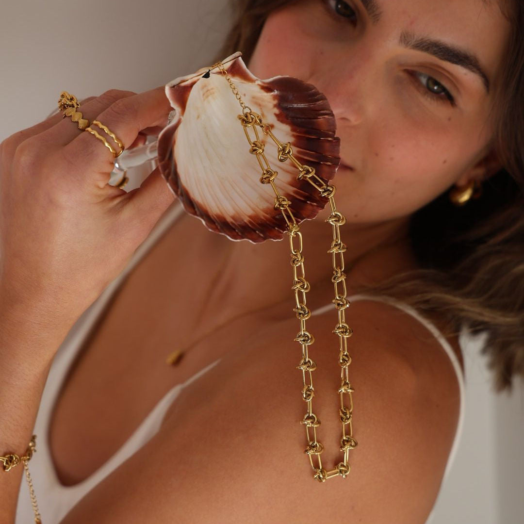 Woman holding a shell with a gold chain and a diamond ring.