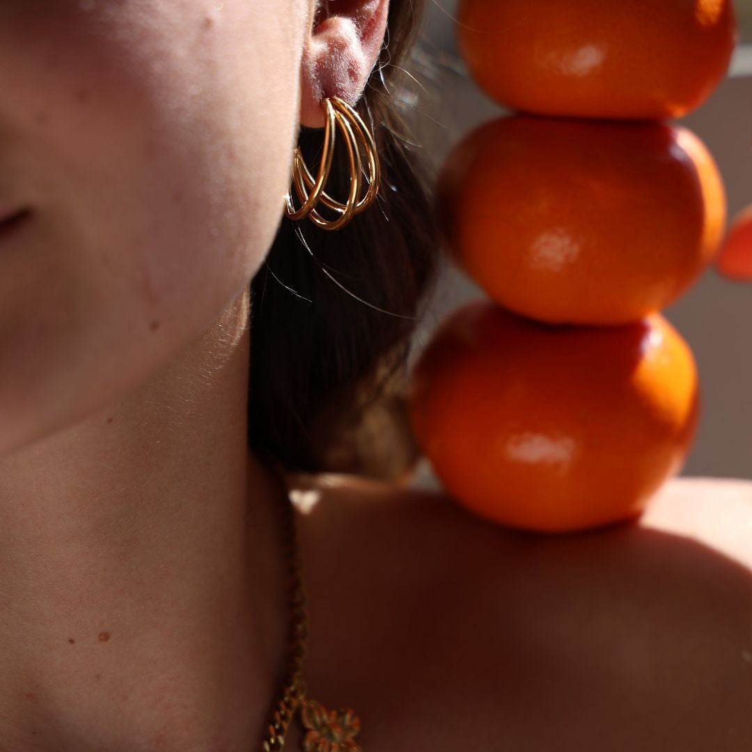 Close-up of a person wearing gold floral jewelry with an orange beaded necklace.