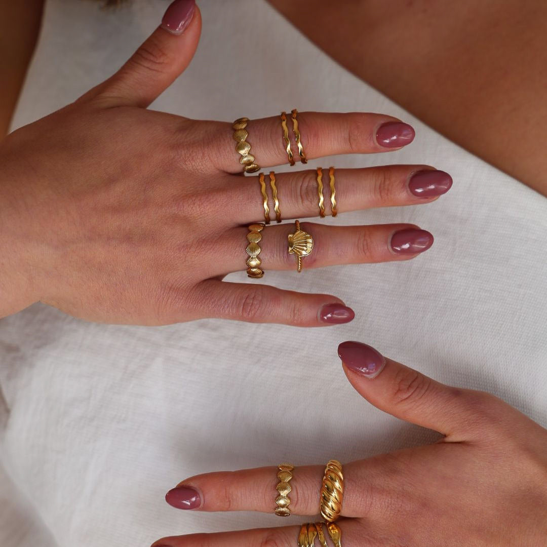 Close-up of hands wearing multiple gold rings on a white background