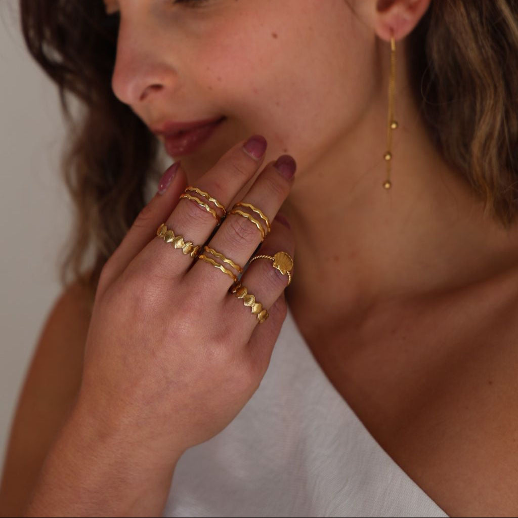 Woman wearing gold earrings and rings with a neutral background
