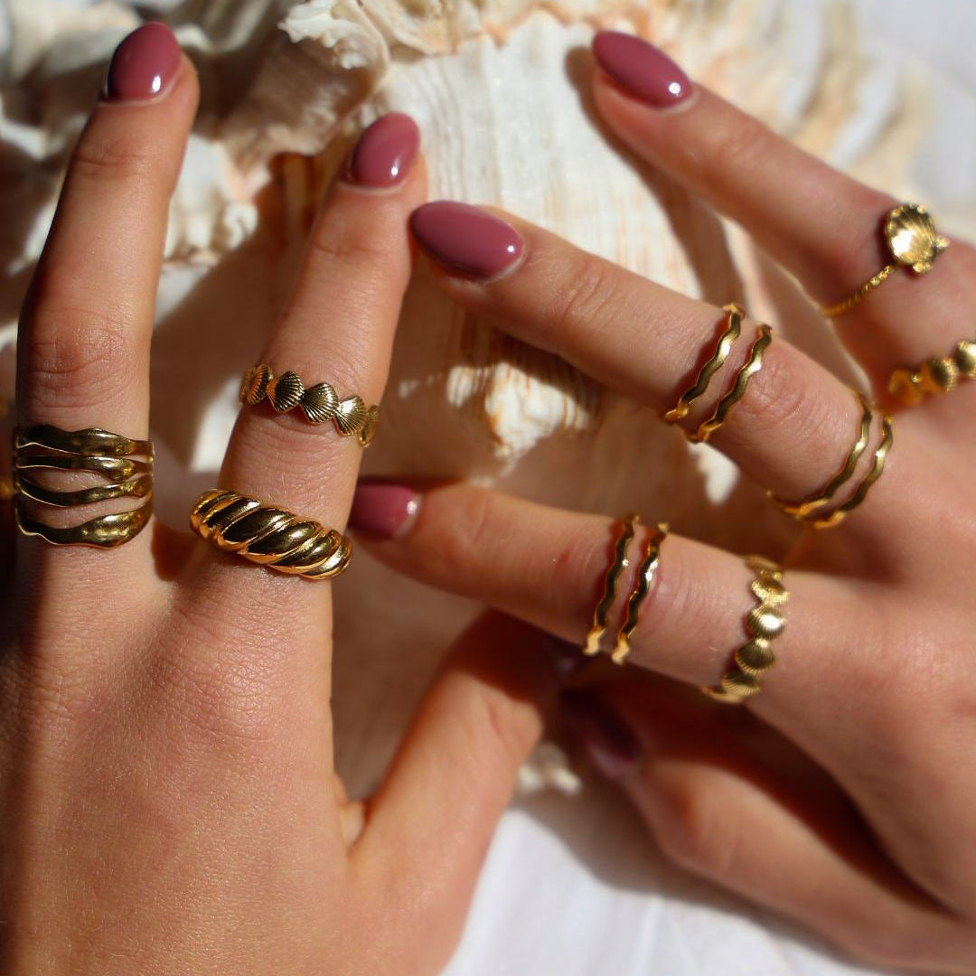 Hands with gold rings and pink nail polish on a white background