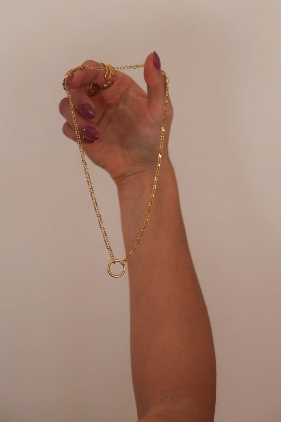 Hand holding a gold necklace against a plain background