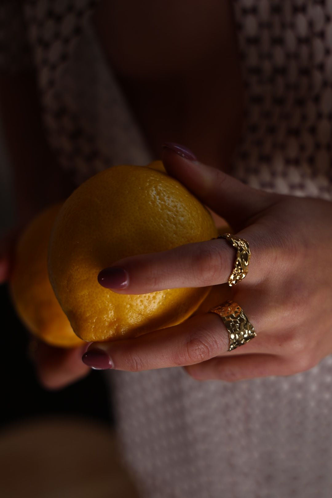 Hand holding a lemon with gold rings on a patterned background