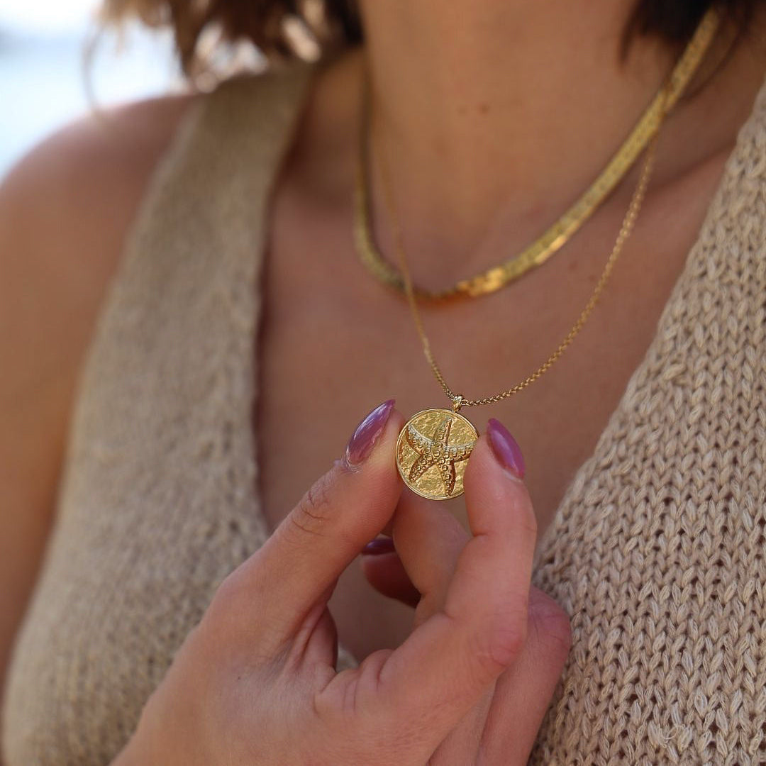 Close-up of a person wearing a gold necklace with a pendant.