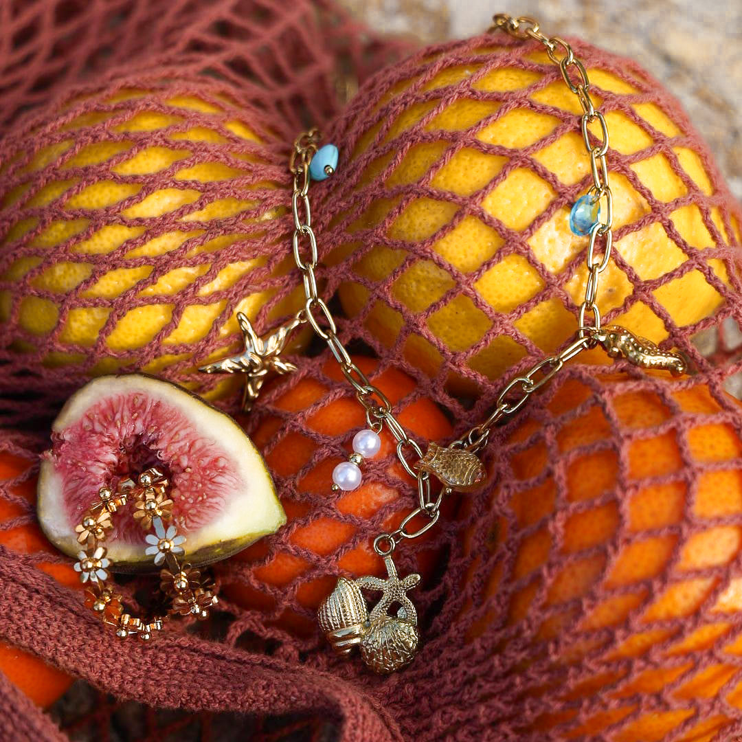 Necklace with charms on a mesh bag with oranges and figs