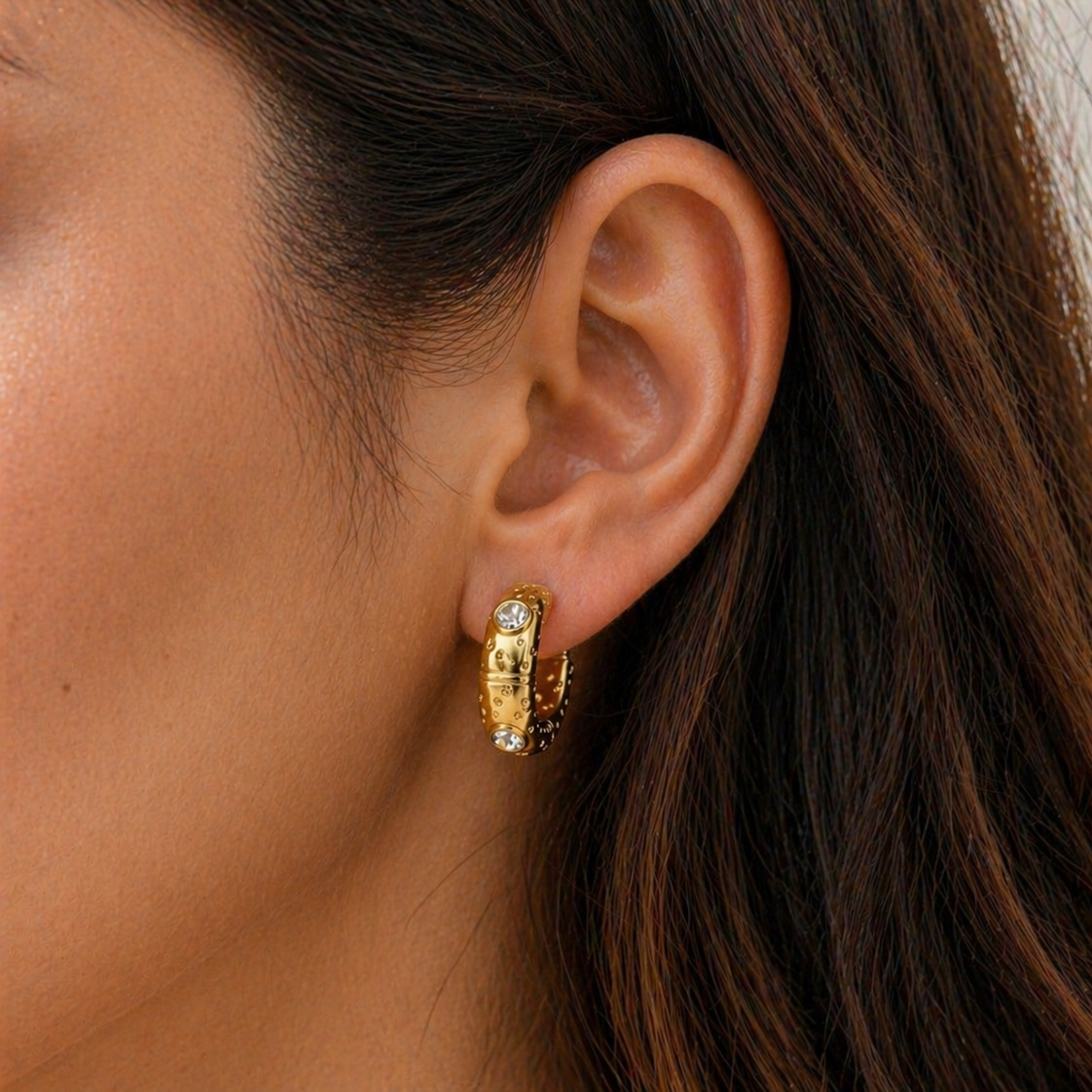 Close-up of an ear wearing gold hoop earrings with a neutral background