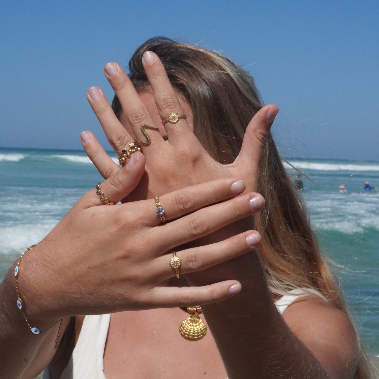 Person holding hands up with multiple rings on fingers against a beach background