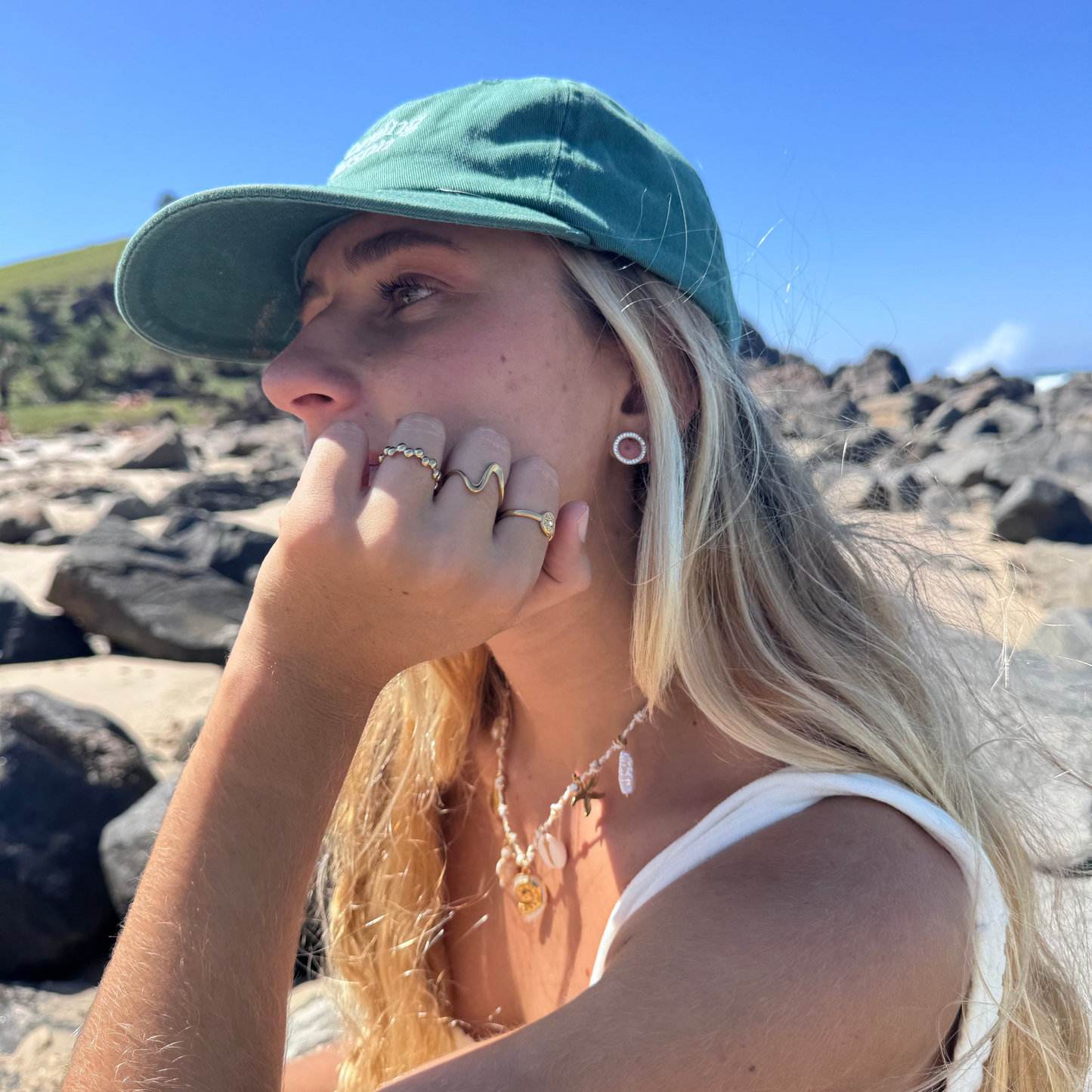 Woman wearing a green cap sitting on rocks with a clear blue sky.