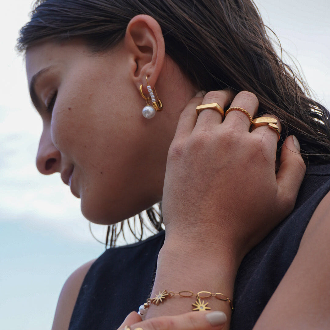 Woman wearing multiple gold rings and earrings with a blurred background