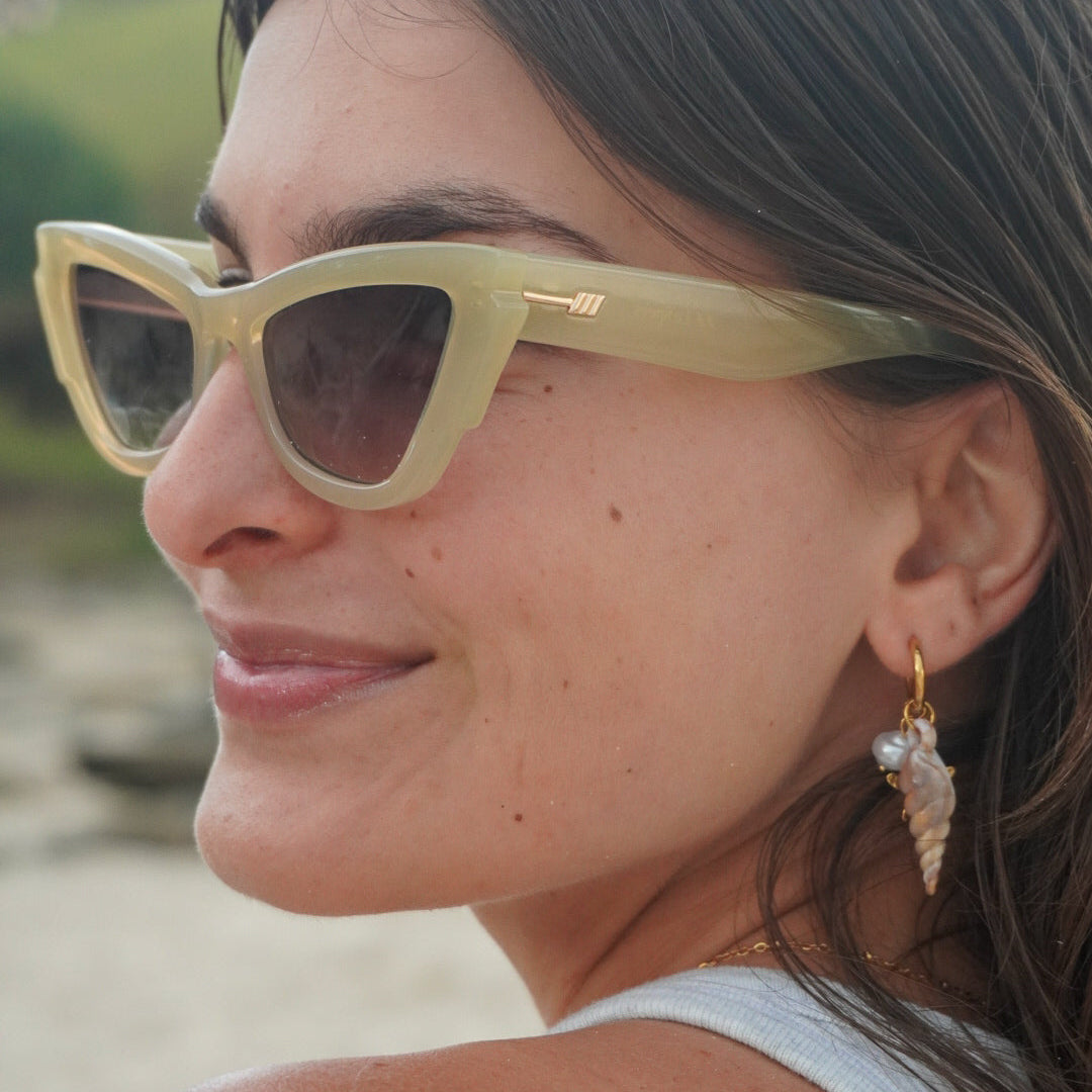 Woman wearing sunglasses and a white top with a blurred natural background