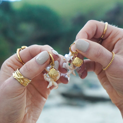 Close-up of hands holding gold and pearl earrings with a blurred natural background
