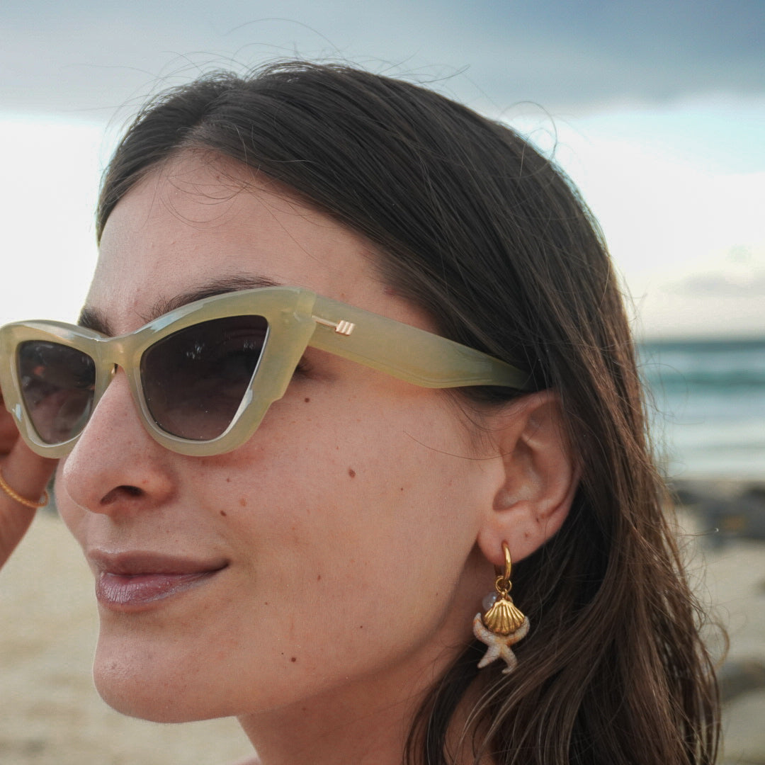 Woman wearing sunglasses on a beach with ocean and sky in the background