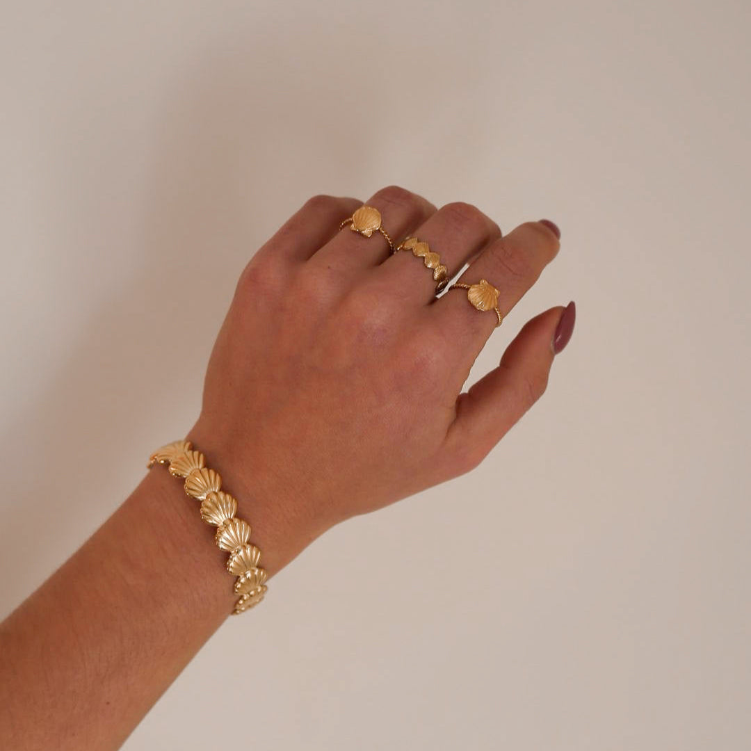 Hand wearing gold bracelets and rings on a plain background
