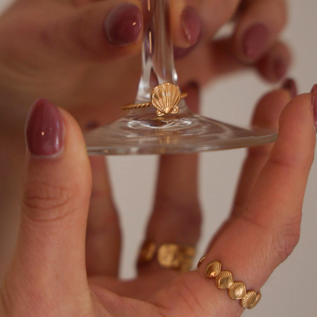 Hand holding a clear glass stand with gold rings on a neutral background