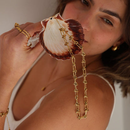 Woman holding a shell with a gold chain and a diamond ring.