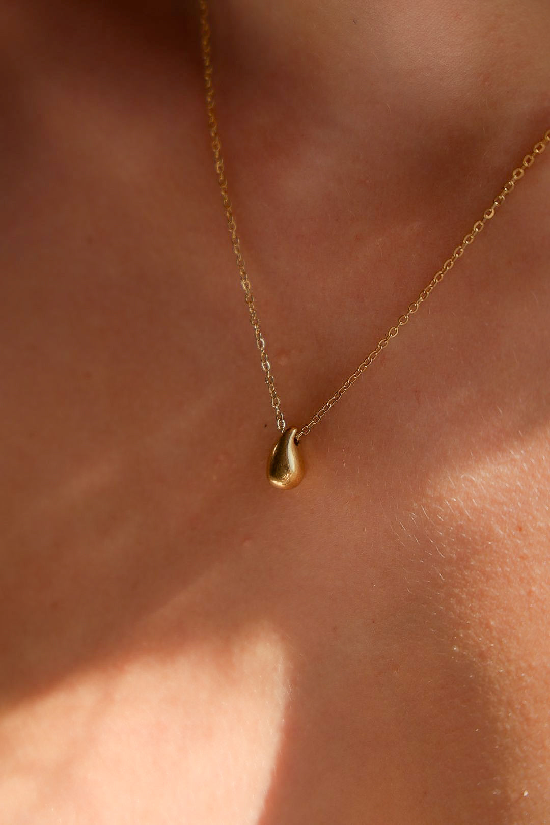 Gold necklace with a teardrop pendant on a person's neck
