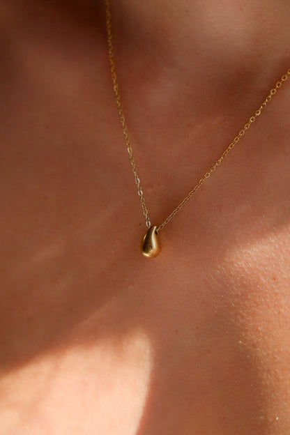 Gold necklace with a teardrop pendant on a person's neck