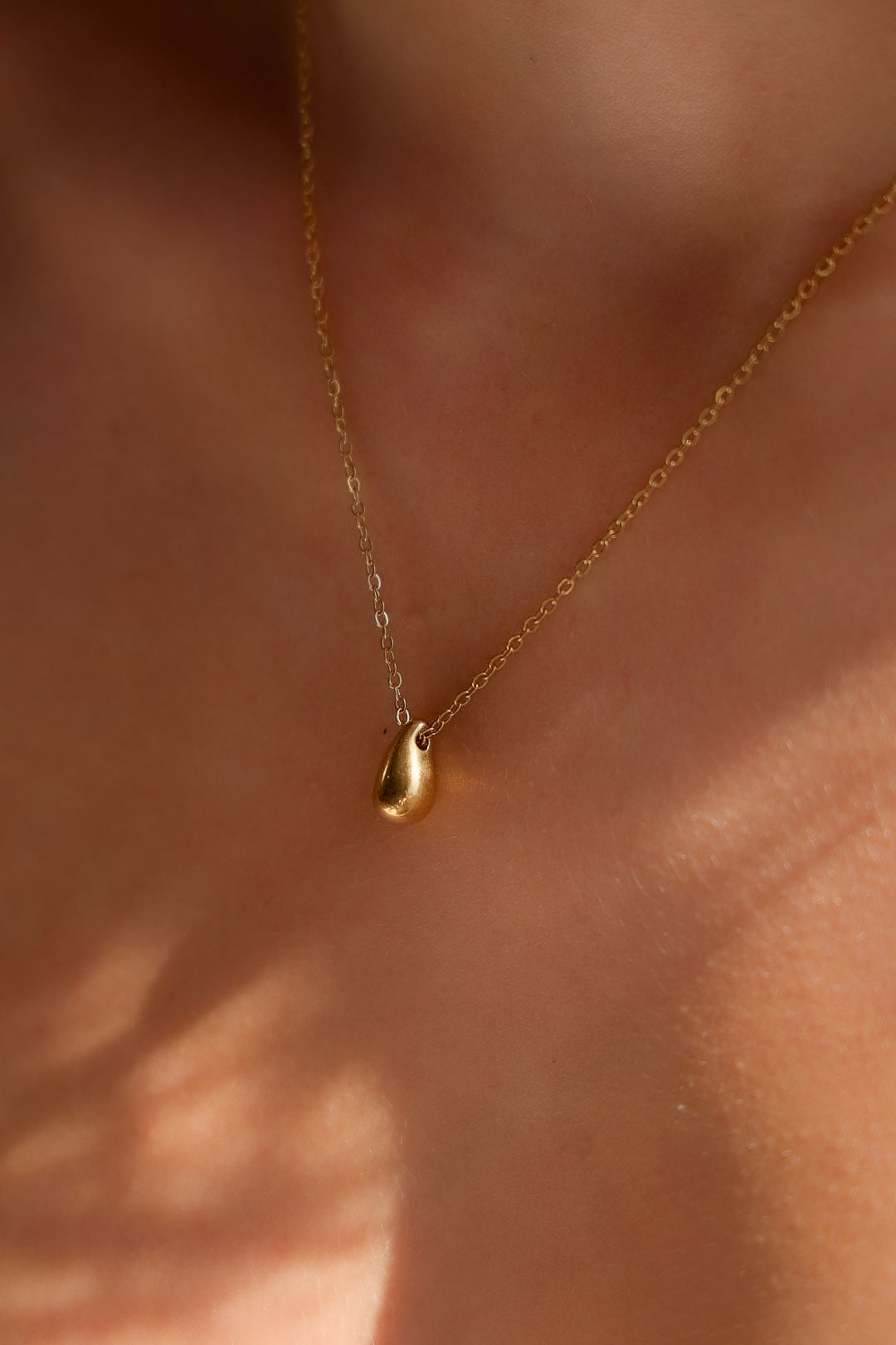 Gold necklace with a small pendant on a person's neck against a neutral background