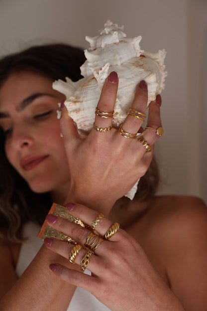 Woman holding a large shell with gold rings on her fingers against a neutral background