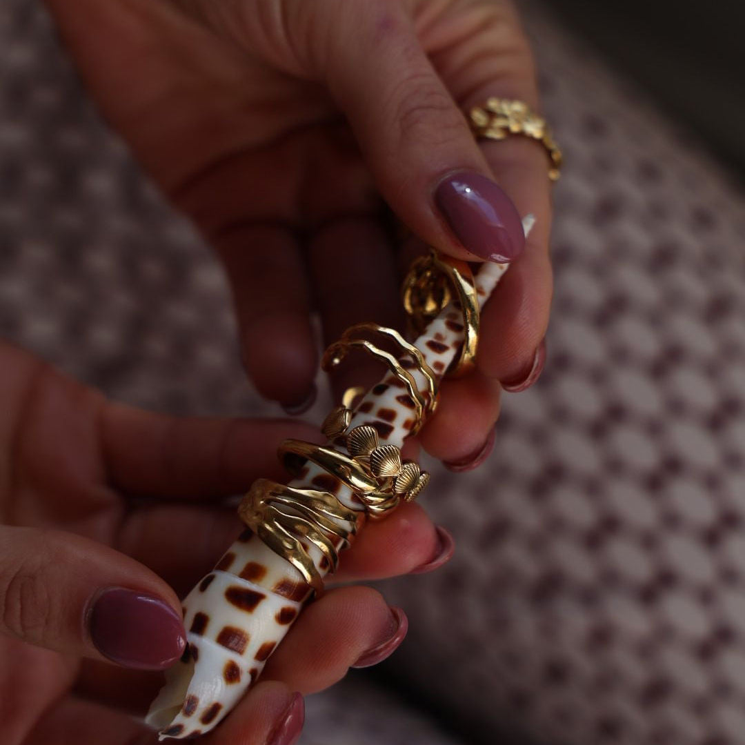 Gold chain wrapped around a shell held by a hand with purple nail polish.