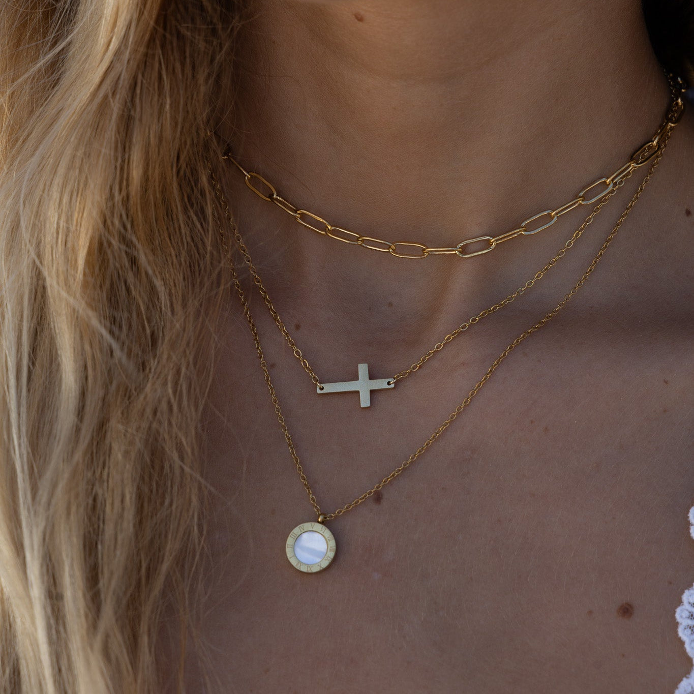 Close-up of a person wearing multiple gold necklaces with a blurred background