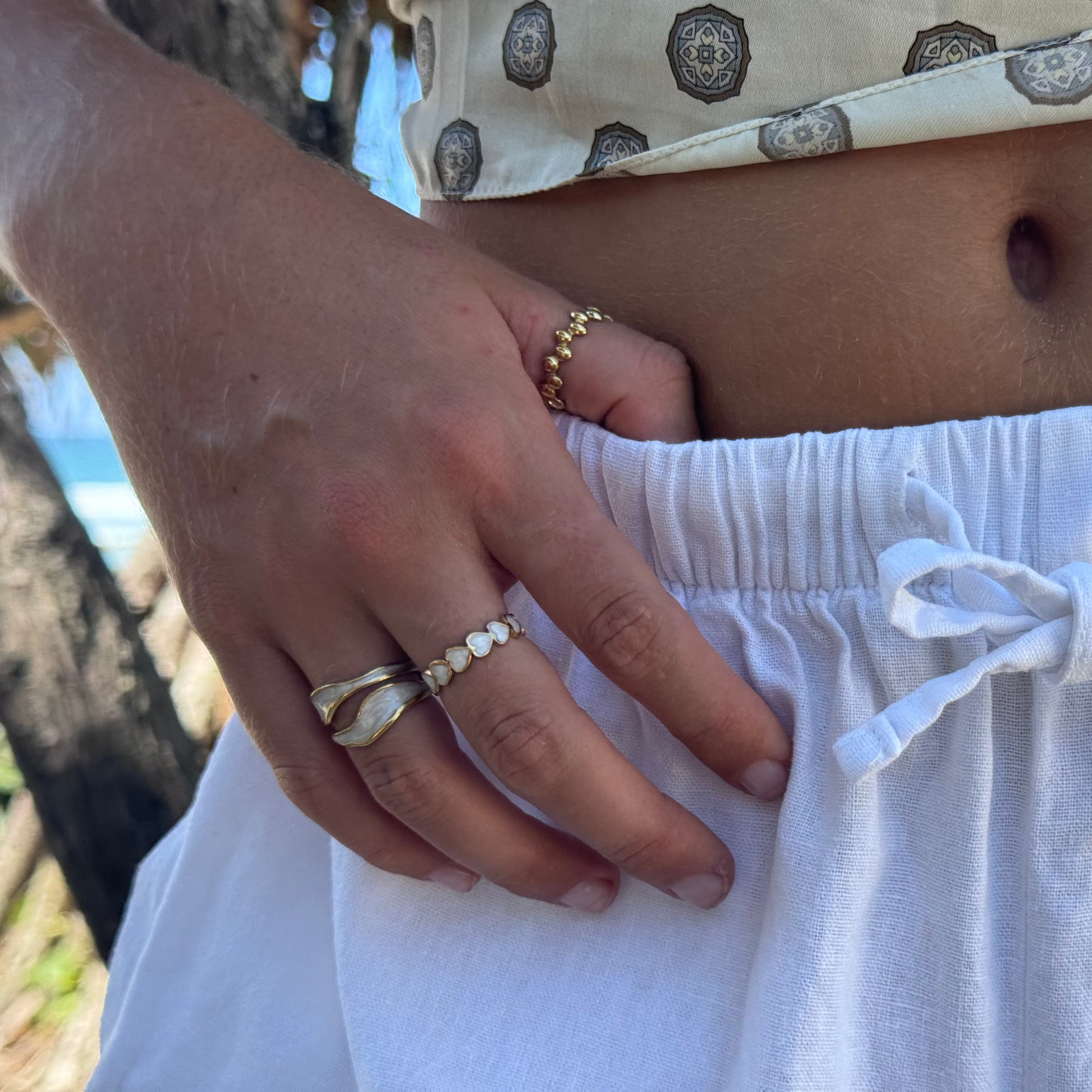 Person wearing a patterned top and white pants with rings on fingers, outdoors.