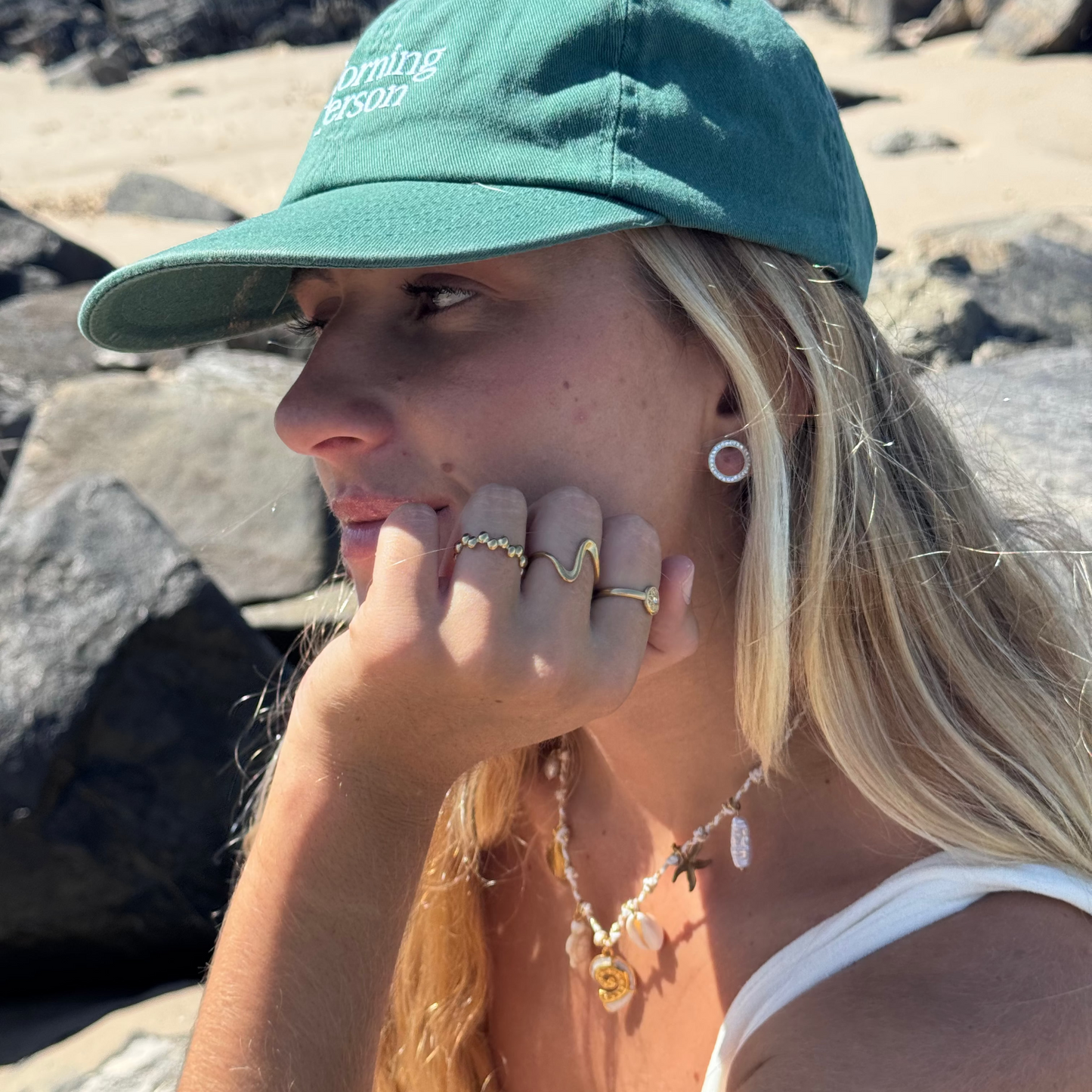 Woman wearing a green cap with text, sitting on rocks outdoors.